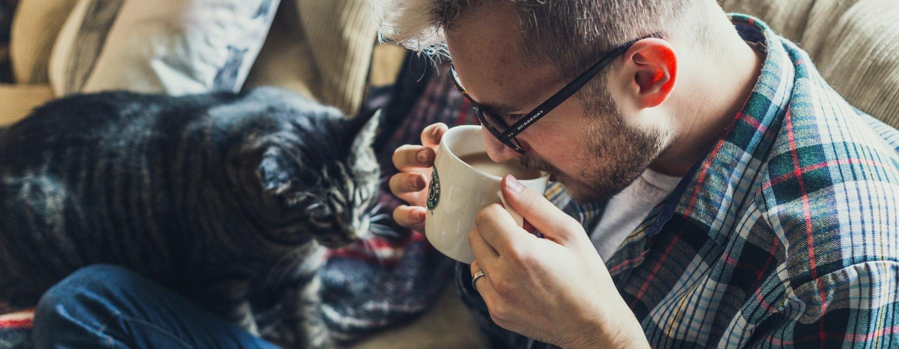 a man drinking from a cup with a cat on his lap